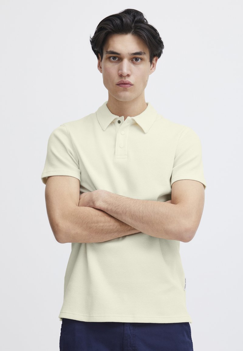 Lys gul teksturert polo-skjorte med korte ermer og krage, med tre knapper ved halsen og rett kant.