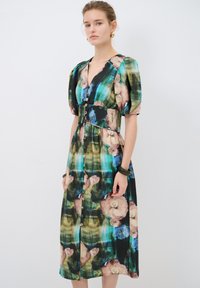 Blumenkleid Midi mit Puffärmeln, V-Ausschnitt und Knopfleiste. Hat ein mehrfarbiges Muster auf schwarzem Hintergrund, taillierte Taille und glattes Material.