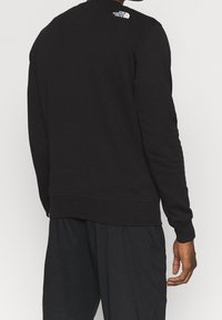 Svart sweatshirt med ribbade muddar och nederkant. Har en liten vit logotyp på övre ryggen. Tillverkad av textilier med struktur. Avslappnad passform.