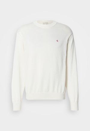 Witte gebreide trui met lange mouwen, geribbelde manchetten en zoom, met een klein rood logo op de borst. Zachte textuur, ronde halslijn.