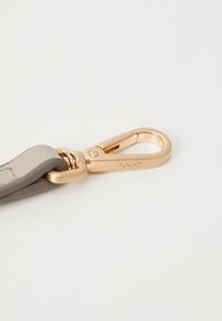 Lys grå læderrem med en guldfarvet metalclip. Remmen har syningsdetaljer. Clippen har et brandet logo på siden.