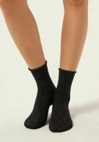 Svarta ankelsockor tillverkade av texturerat tyg, något glittriga med ribbad kant, som sitter tätt runt anklarna och fötterna.