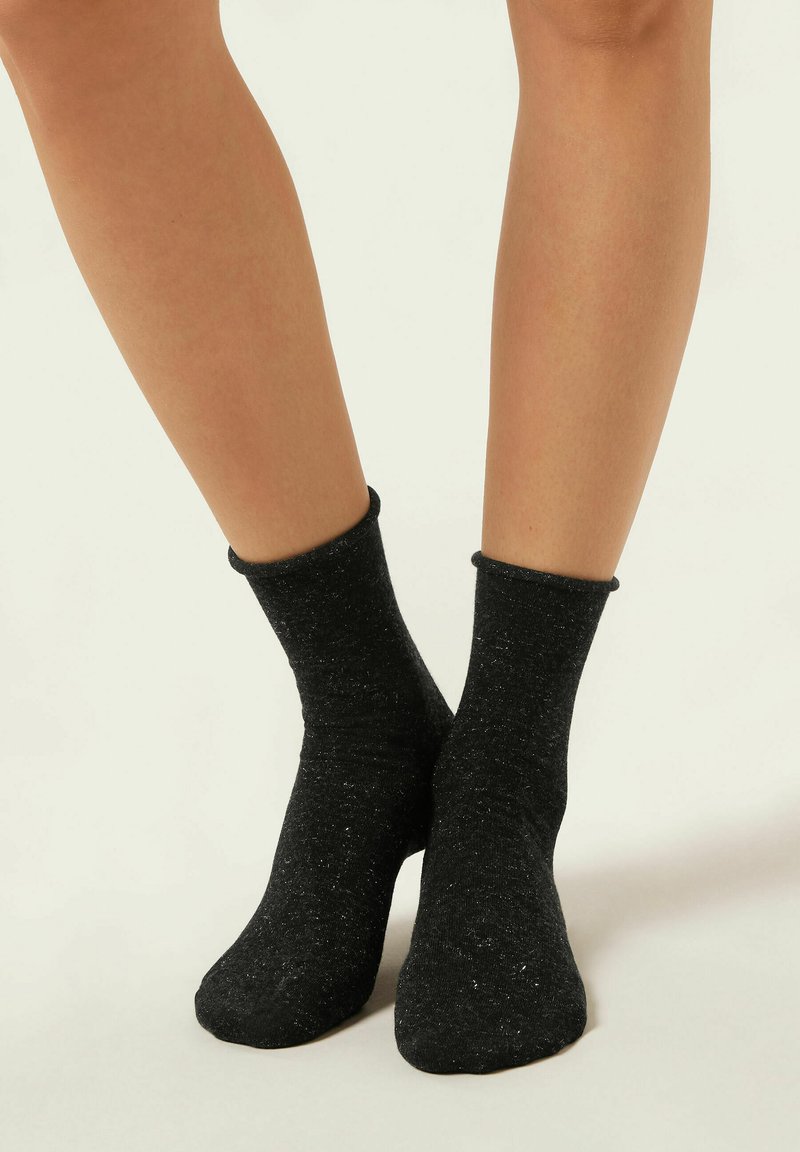 Svarta ankelsockor tillverkade av texturerat tyg, något glittriga med ribbad kant, som sitter tätt runt anklarna och fötterna.