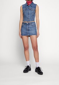 Denimväst och kjolset, ljusblå tvätt, strukturerad design, synliga sömmar, fickdetaljer, ihopparat med svarta platåskor och vita strumpor.