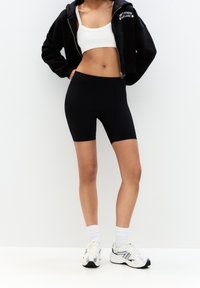 Czarne dopasowane szorty z wysokim stanem, wykonane z elastycznego materiału, zestawione z białym topem na krótki rękaw i czarną bluzą z zamkiem.