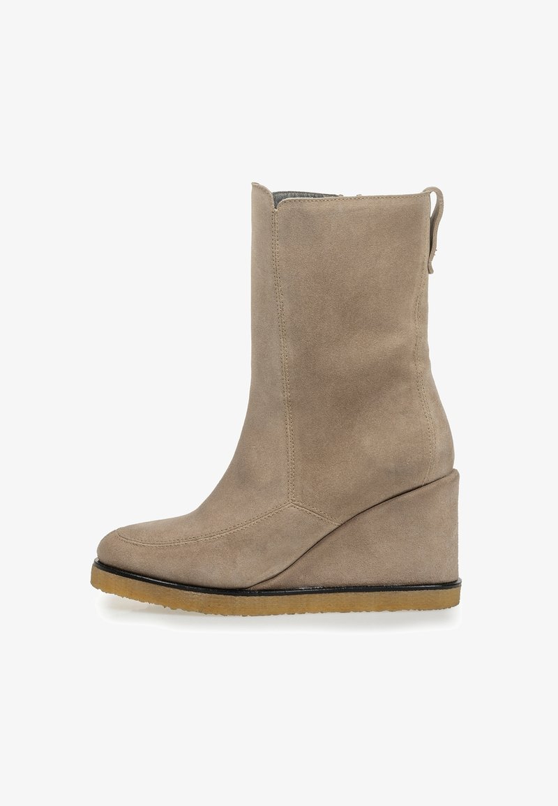 Botín de tobillo de ante beige con cuña, punta redonda y suela texturizada. El diseño incluye un tirador en la parte trasera y costuras sin costura.