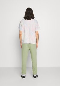 Flerfärgad t-shirt med kort ärm och marmorliknande mönster, matchad med gröna sweatpants och svarta sneakers, sedd bakifrån.