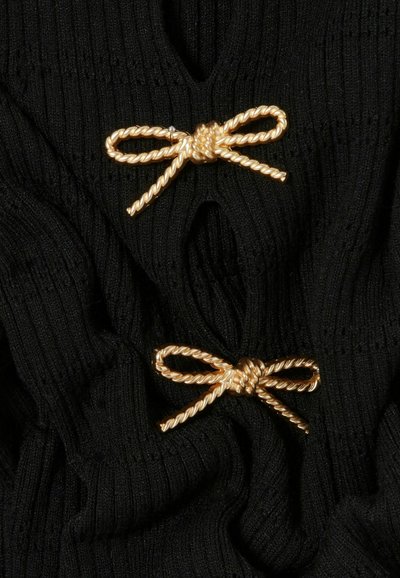 Due fibbie a forma di fiocco in metallo color oro attorcigliato su un tessuto a coste nero, che bloccano o decorano il capo.
