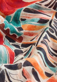 Tissu avec motif abstrait multicolore de coups de pinceau en bleu sarcelle, orange, rouge, noir et beige avec texture et plis visibles.