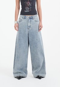 Jasnoniebieskie dżinsy z szerokimi nogawkami i wysokim stanem, wykonane z denimu. Posiadają duże kieszenie i wyblakły kolor. Połączone z czarną dopasowaną bluzką.