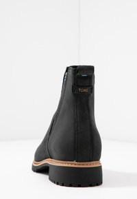 Bottines en suede noir avec une surface texturée, des panneaux latéraux élastiques et une semelle marron contrastante. Présente un petit logo à l'arrière.