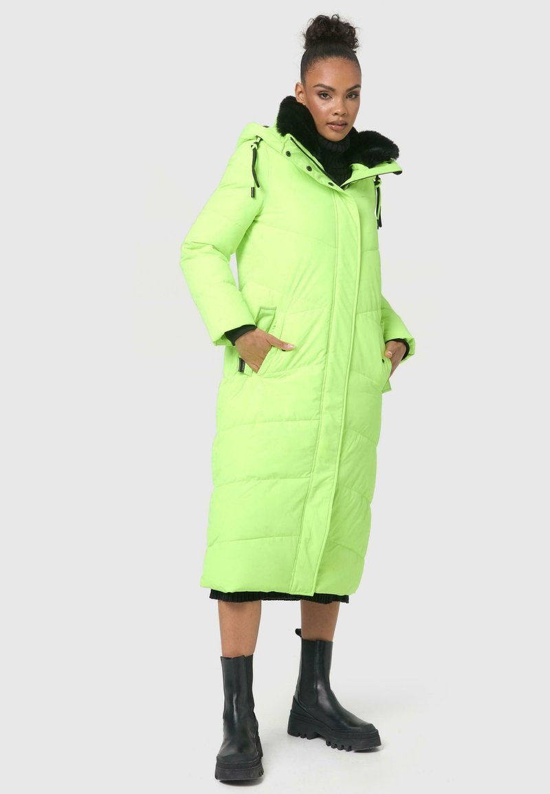 Lang, gewatteerde jas in fel neon groen met een nep bontkraag, zijzakken en een rechte zoom. Draagt over een zwarte turtleneck en zwarte laarzen.