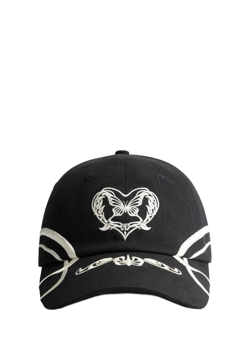Black cap with white decorative embroidery featuring a heart and butterfly design. Accented with white stripes along the visor. Cotton material.