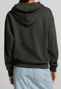 Felpa grigia scura con un grande cappuccio, polsini a costine e orlo, caratterizzata da una vestibilità morbida e una texture soffice, abbinata a una gonna di jeans chiari.