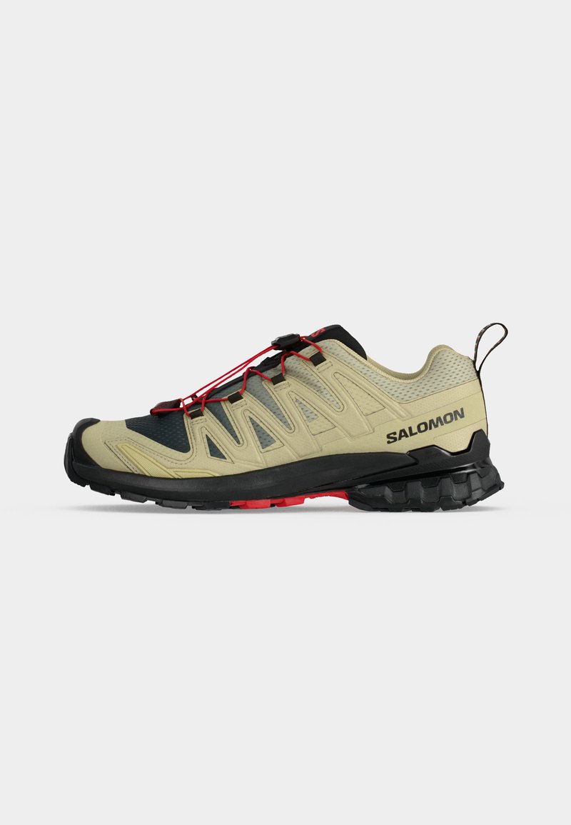 Chaussure de trail Salomon beige et noire avec des lacets rouges et une semelle noire robuste, vue de côté sur fond blanc.