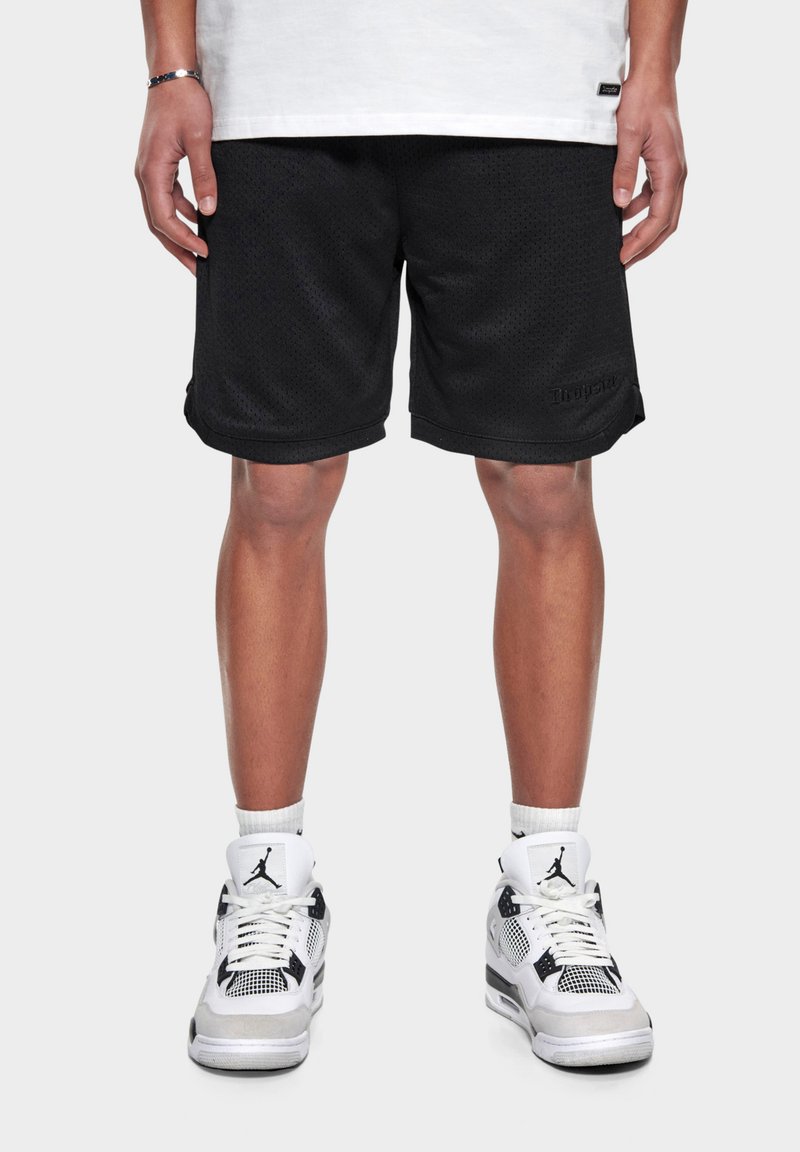 Sorte mesh atletisk shorts med en løs pasform, der har et lille logo på kanten. Båret med hvide og sorte sneakers.
