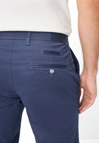 Pantaloni in blu navy di tessuto testurizzato con una tasca posteriore bottone e un piccolo etichetta in vita, caratterizzati da dettagli di cucitura precisi.