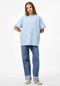 Gaišzils pārāk liels T-krekls ar apaļu kakla izgriezumu, apvienots ar brīviem džinsu biksēm ar saplēstām malām un gaiši zilu aproci.