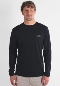 T-shirt noir à manches longues en tissu doux, avec un petit logo blanc sur la poitrine, col rond et coupe décontractée.