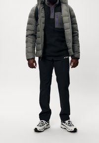 Grå pufferjakke med en sort fleecepullover og sorte bukser; har lilla lynlåse og hvide sneakers med sorte såler.