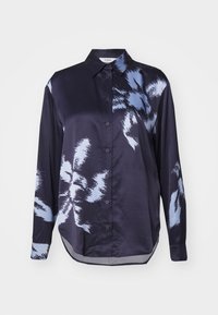 Chemise en soie bleu marine à manches longues, fermeture à boutons sur le devant, avec un motif floral abstrait bleu sur le côté gauche. Ourlet et col arrondis.