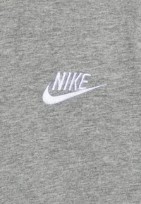 Grå bomullsskjorte med en hvit brodert Nike-logo på venstre side, med en glatt tekstur og avslappet design.
