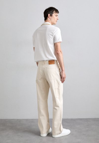 White polo shirt with a yellow collar, beige cargo pants, and white sneakers. The pants feature side pockets and a leather label at the waist.