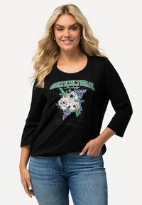 Camiseta de manga larga negra con un diseño gráfico floral. El diseño incluye flores blancas con hojas verdes y el texto "Sociedad Horticultural".