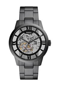 Montre en acier inoxydable noir avec un cadran transparent affichant un mouvement automatique en argent, des accents dorés et des index horaires en chiffres romains.