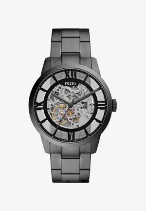 Black stainless steel watch with transparent face displaying a silver automatic movement, gold accents, and Roman numeral hour markers.