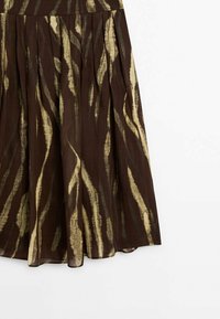 Bruine geplooide rok met een contrasterend abstract patroon in crème en goud, gemaakt van lichte stof, met een gladde textuurafwerking.