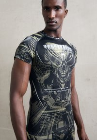 Short-sleeved athletic shirt in black with green graphic print depicting a skull and technical designs, featuring white text and accents.