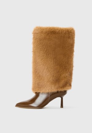 Brown leather high-heeled boot with a tall, fuzzy brown faux fur shaft. Pointed toe and slim stiletto heel. Smooth texture contrasts with fur.