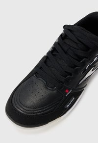 Black athletic shoe featuring a textured leather upper, flat laces, perforated sections, and a white accent on the sole with a "REACTIVE" label.