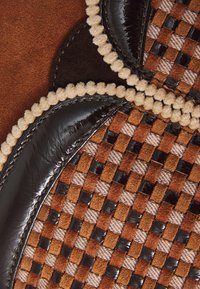 Tessuto intrecciato con un motivo a quadri nei colori marrone, arancio e beige, con unto accentato in pelle nera lucida e bordo in pompon beige.