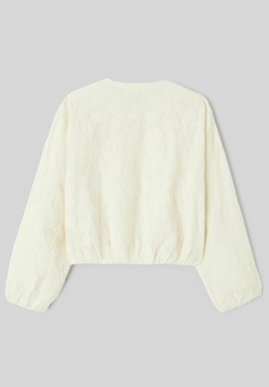 Blouse courte à manches longues de couleur crème avec une texture florale subtile et un ourlet ainsi que des poignets élastiqués, posée à plat sur un fond gris.