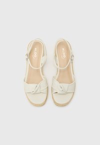 Šviesiai bežinės espadrilės su mazgo akcentu, minkšta medžiaginė viršutinė dalis, reguliuojamas kulkšnies dirželis ir nertas jūratvarkos platformos padas.
