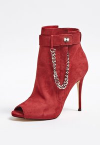 Bottine à talon haut en daim rouge avec bout ouvert, bride à la cheville ornée de clous argentés, et détail décoratif de chaîne argentée.
