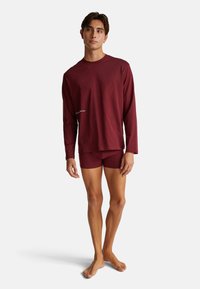 Bordová košile s dlouhým rukávem a odpovídajícími šortkami. Hladký, elastický materiál s mírným leskem. Minimalistický design, logo potištěné na košili.