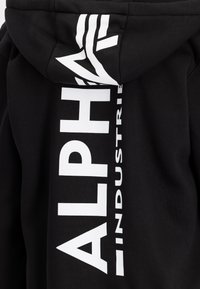Sort hætte sweatshirt med et vertikalt hvidt logo på ryggen. Lavet af blødt, tekstureret stof, med snøre i hætten og en afslappet pasform.