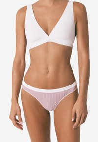 Bralette bianco con scollo a V e spalline spesse, abbinato a un costume da bagno con stampa a righe rosse e bianche caratterizzato da un elastico bianco in vita.