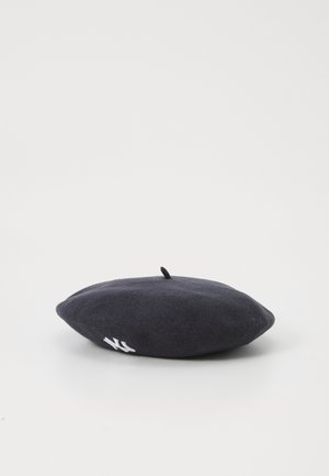 Beret negro de fieltro con una textura suave, forma redondeada, con un pequeño lazo en la parte superior y un detalle de logo bordado en blanco a un lado.