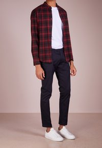 Rood en zwart geruit flanellen shirt over een wit T-shirt, in combinatie met donkere slim-fit broeken en witte sneakers.