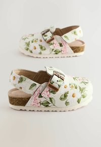 Blumen-Clogs mit einem weißen, glatten Lederoberteil, das mit pinken und grünen Blumenmustern, einer metallischen Schnalle und einer strukturierten beigen Sohle ausgestattet ist.