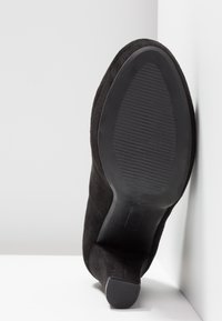 Escarpin en suede noir à talon haut avec un bout pointu lisse, une semelle texturée et une silhouette élégante. Le talon est droit et robuste.