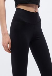 Μαύροι ψηλόμεσοι κολάν από ελαστικό, λείο ύφασμα. Διαθέτουν φαρδιά ζώνη μέσης και εφαρμοστή σχεδίαση, κατάλληλοι για αθλητική χρήση.