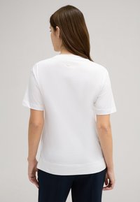Witte korte mouwen t-shirt van katoen, met een ronde halslijn en een klein logo-detail op de bovenrug. Zachte textuur, relaxte pasvorm.