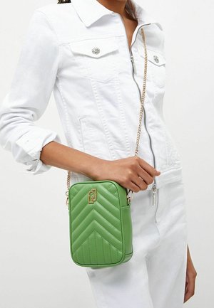 Sac bandoulière vert matelassé avec motif en chevron, garnitures dorées et bandoulière en chaîne. Le sac a une forme rectangulaire et une texture lisse.