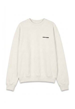 Man draagt een witte sweater met de tekst "PEGADOR" op de borst en een zwarte broek met een bijpassend logo op het bovenbeen, rechtopstaand.