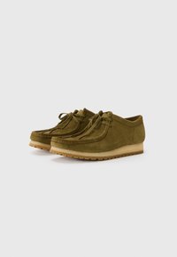 Zapatos de ante verde oliva con un perfil bajo, que cuentan con la puntera redonda, borlas y una suela de goma ligera con detalles texturizados.